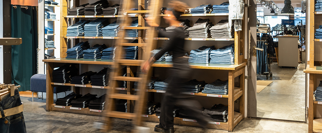 Beraterin geht am Jeansregal vorbei Beraterin geht am Jeansregal vorbei